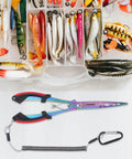 Front view of iridescent stainless steel long-nose fishing pliers with lanyard beside a tackle box filled with lures