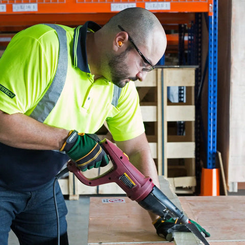 Worker using a power tool on wood wearing high-visibility shirt and safety glasses in warehouse