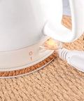 Close-up of Electric Ceramic Tea Kettle With 1 Liter Capacity showing auto shut off feature and power cord on a woven base.