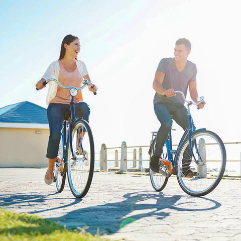 Two people riding comfort bikes on a sunny day near the beach boardwalk.