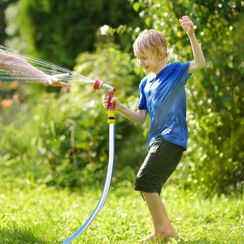 Garden hose, blue with red spray nozzle, held by child while spraying water in a sunlit backyard.