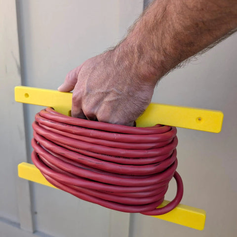 Hand holding Heavy Duty Extension Cord Reel and Yellow Cord Organizer with red cord wrapped, ideal for quick wraps on wall or workbench.