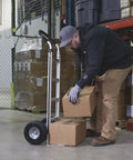 Man using Aluminum Hand Truck With 600 Pound Capacity For Moving Boxes And Crates, Continuous Flow Handle, Smooth Rolling Ten Inch Polyurethane Wheels, Seven And A Half Inch Toe Plate in warehouse