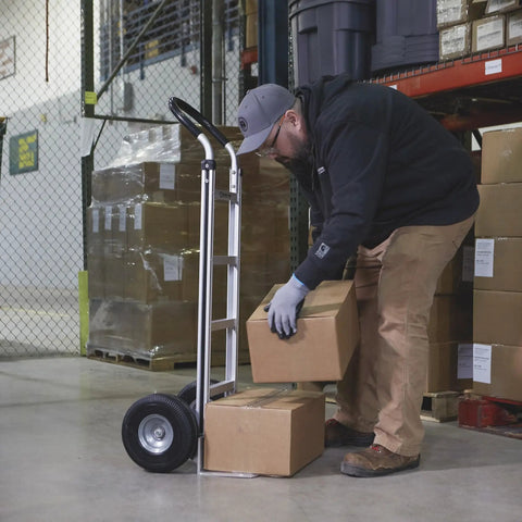 Man using Aluminum Hand Truck With 600 Pound Capacity For Moving Boxes And Crates, Continuous Flow Handle, Smooth Rolling Ten Inch Polyurethane Wheels, Seven And A Half Inch Toe Plate in warehouse