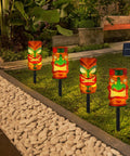 4 Pack Solar Tiki Light Decor Waterproof Tiki Statues installed in garden, glowing at night, for Outdoor Hawaiian Party and garden ambience.