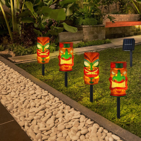 4 Pack Solar Tiki Light Decor Waterproof Tiki Statues installed in garden, glowing at night, for Outdoor Hawaiian Party and garden ambience.