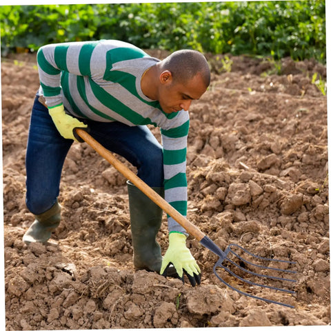 Man using heavy duty handheld manure fork for farming and gardening in soil, solid iron tool for composting and agriculture work.