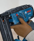 Gutsy 18 Volt Brushless Cordless Brad Nailer Kicks Out 2,000 Nails Per Charge held in hand with glove, showing safety trigger and design.