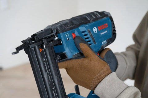 Gutsy 18 Volt Brushless Cordless Brad Nailer Kicks Out 2,000 Nails Per Charge held in hand with glove, showing safety trigger and design.