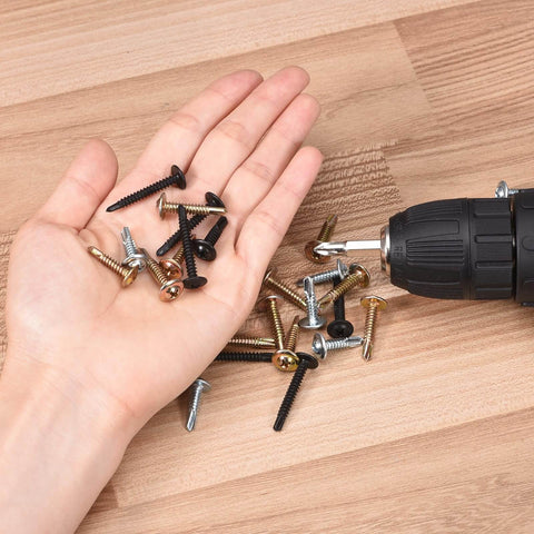 Hand holding various small screws and drill on wooden surface
