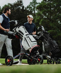 Two men conversing on golf course next to Nitron Golf Push Cart With Auto Open Technology and Top Lok System in black and slate finish.