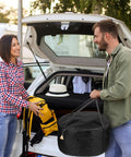 Couple with a car trunk loading a Beefy Heavy Duty Water Resistant Carrying Bag For 19 Inch Outdoor Propane Fire Pit