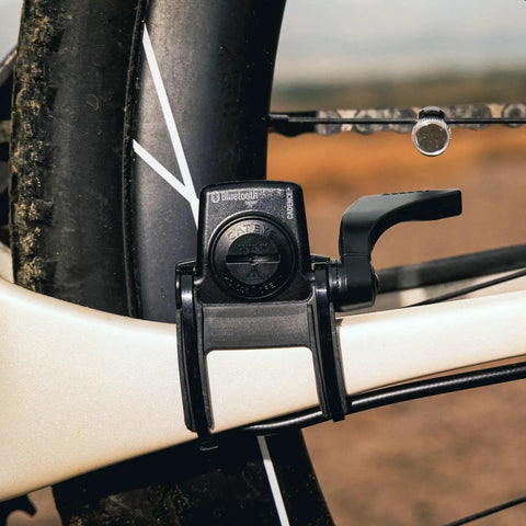 Close-up of Padrone Digital Bluetooth Cycling Computer With IPX8 Waterproof Build attached to a bike frame near the rear wheel.