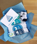 Baby gift set with blue nautical theme, including onesies for 2-4 months, blue pacifier, socks, and card in blue tissue paper.