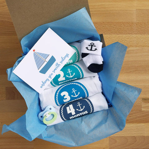 Baby gift set with blue nautical theme, including onesies for 2-4 months, blue pacifier, socks, and card in blue tissue paper.