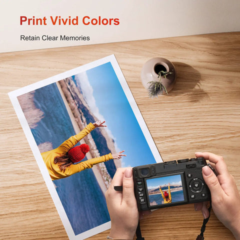 Person holding camera with photo print on table showing colorful landscape and person in yellow jacket, titled 'Print Vivid Colors'.