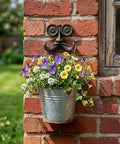 Heavy Duty Kickass Cast Iron Mustache Wall Hooks holding a flower pot on a brick wall, ideal for outdoor decor.
