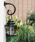 Outdoor black metal lantern on hook mount with greenery, part of 4 Pack Metal Landscape Lighting Mounting Brackets With 3/4-14NPSM Threads For Tree Deck And Wall Mounts
