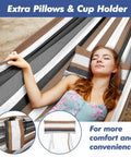 Woman relaxing in a 550 Pound Capacity Double Hammock With Stand In Desert Stripe Portable Bag Included Ultra Comfortable 60 By 80 Inch Cotton Polyester Bed Easy Setup For Two And Backyard Chill, with extra pillows and cup holder.