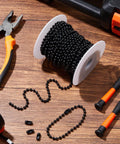 Black 50ft beaded chain for roller shades and vertical blinds with 50 connectors on spool, surrounded by tools on wood surface.