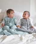 Two babies sitting on a bed wearing Supersoft Wearable Baby Sleep Sack Made From Bamboo Viscose 1.5 TOG 6 To 12 Months Medium Calm Sage