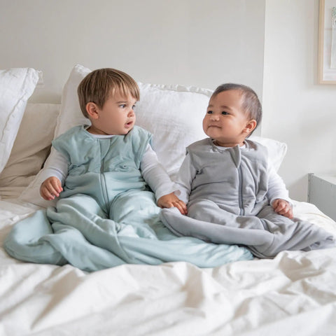 Two babies sitting on a bed wearing Supersoft Wearable Baby Sleep Sack Made From Bamboo Viscose 1.5 TOG 6 To 12 Months Medium Calm Sage