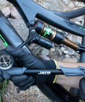 Cyclist using ShockPro MTB Shock Pump With 300 PSI High Pressure Gauge on rear shock of mountain bike, on rocky terrain.