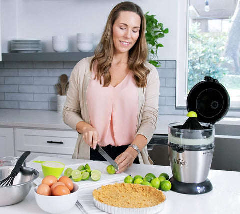 Compact Automatic Citrus Juicer With Hands Free Electric Press For Fresh Orange Lemon Lime Extract on kitchen counter with limes.