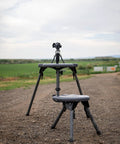 Stable Table Lite With Weatherproof Tabletop And Ambidextrous Seat fully set up on a gravel path with rifle bipod support