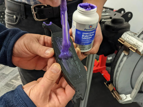 Permatex Ceramic Extreme Brake Parts Lubricant, 8 oz bottle, applied to a brake pad (close-up view)