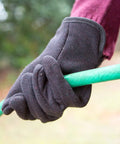 Close-up of hand wearing Brown Jersey Winter Work Gloves with Red Fleece Lining gripping a green garden hose outdoors