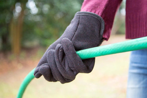 Close-up of hand wearing Brown Jersey Winter Work Gloves with Red Fleece Lining gripping a green garden hose outdoors