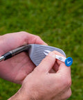 Hand holding a Premium Slick Rubberized Golf Tee with a durable plastic base, preparing to tee up a golf ball on the course.