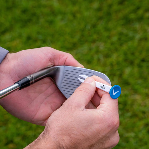 Hand holding a Premium Slick Rubberized Golf Tee with a durable plastic base, preparing to tee up a golf ball on the course.