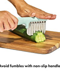 OXO Tot crinkle cutter for baby feeding, mint green handle with stainless steel blades cutting cucumber on a board