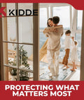 A family embracing near a large window with Kidde logo and slogan 'Protecting What Matters Most' in a bright living room.