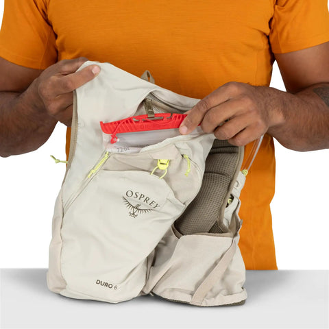 Man holding Duro 6L Running Hydration Vest with Hydraulics Soft Flasks in sandy grey, showing front pockets and stabilizers