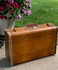 Vintage suitcase with two brown leather luggage handles with metal mounts installed, shown on a patio near flowers.