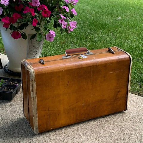 Vintage suitcase with two brown leather luggage handles with metal mounts installed, shown on a patio near flowers.