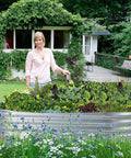 Woman standing beside Galvanized Raised Garden Bed Kit Oval 4x2x1 Ft Outdoor Planter Boxes for Vegetables in a garden