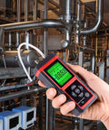 Close-up of red and black digital manometer held in hand with green LCD display, connected to HVAC piping.