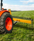 60 Inch Heavy Duty Powder Coated Steel Pine Straw Rake With 26 Spring Steel Tines attached to red tractor on grass field