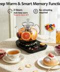 Glass electric tea maker with infuser, displaying herbal tea brewing; tea set on table with fruit and pastries