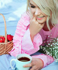 Woman in pink dress holding a coffee cup with a picnic basket of strawberries on a blue blanket outdoors.