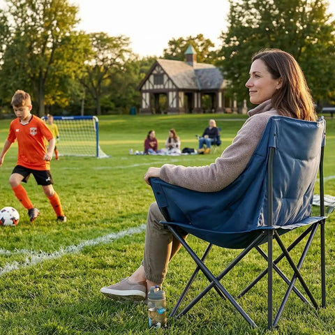 Woman sitting on heavy duty portable camping chair with 350 lb capacity next to a soccer field, focus on ergonomic padded seat.