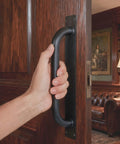 Person gripping Beefy 12 Inch Heavy Duty Steel Barn Door Handles Black Powder Coat 2 Pack Gate Pulls on wooden door