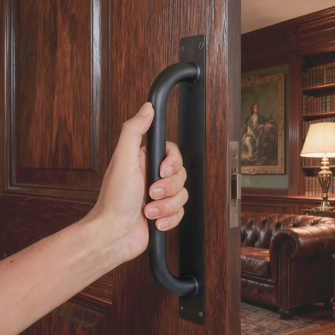 Person gripping Beefy 12 Inch Heavy Duty Steel Barn Door Handles Black Powder Coat 2 Pack Gate Pulls on wooden door