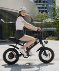 Person riding black 16 Inch Fat Tire Electric Bike For Adults And Teens With Peak 1500W Motor 28 MPH Top Speed 65 Mile Range 48V 15.6Ah Battery Full Suspension All Terrain Ebike For Mountains Snow And Sand Black in urban setting.