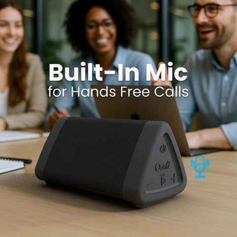 Angle 3 4th Gen Portable Bluetooth Speaker With 12W Stereo Sound 24 Hour Playtime Rich Bass 100 Foot Wireless Range Waterproof shown on desk in meeting room with built-in mic for hands-free calls.
