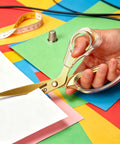 Go-To Everyday Office And Craft Scissors With Titanium Coated Blades And Clear Ergonomic Handles, Durable 3 Pack For Home Desk Or School Projects, Gold Finish For Sharp Clean Cuts. Hand holding gold scissors cutting paper.